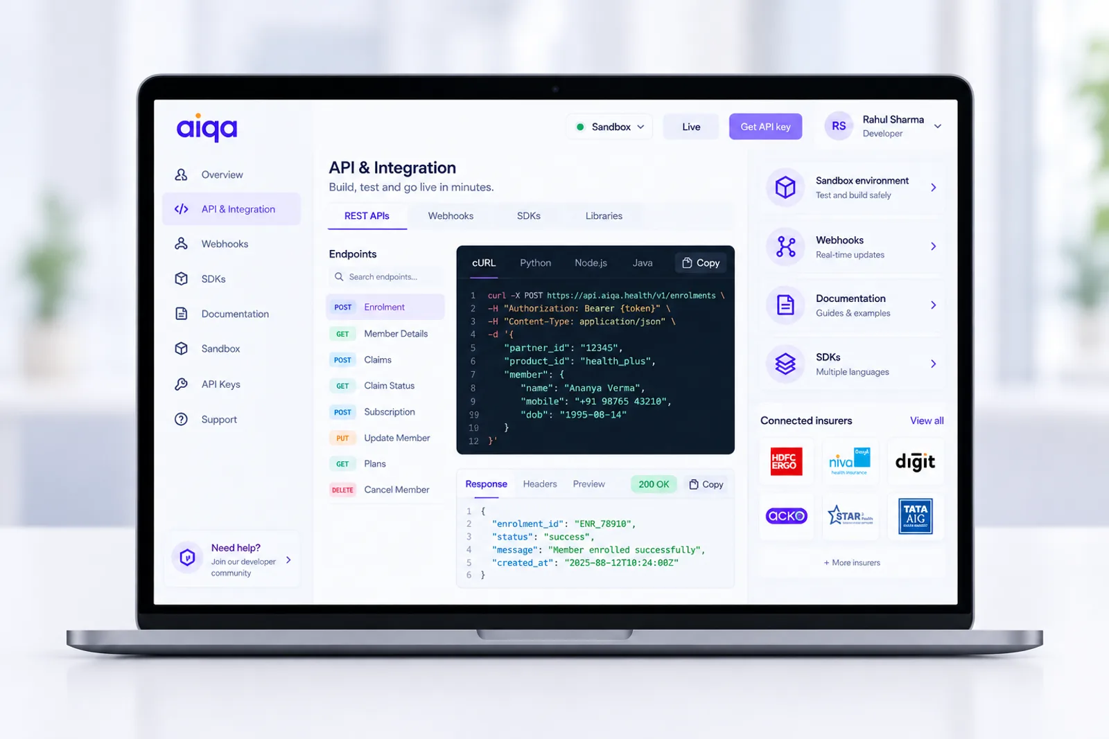 The aiqa developer console on a laptop: an enrolment request with its response beneath, a sandbox and live environment switch, webhooks and SDKs, and the connected insurers below.